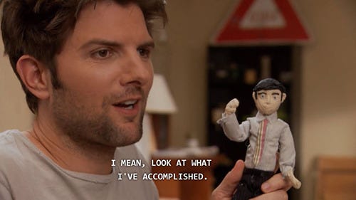 Ben Wyatt from Parks and Rec holding up a little doll he made with the caption "I mean, look at what I've accomplished."