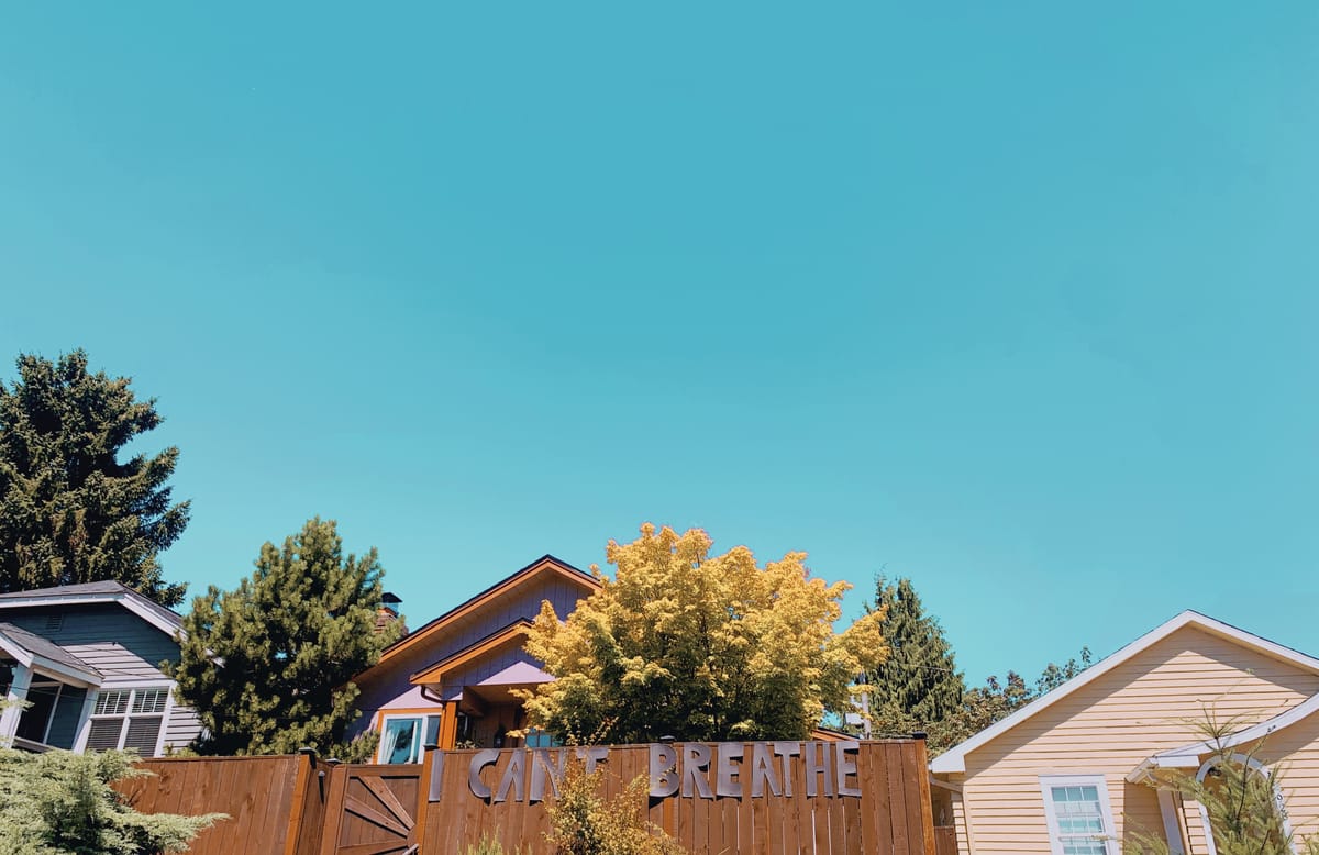 a neighborhood with a blue sky and the words "i can't breathe" on a fence